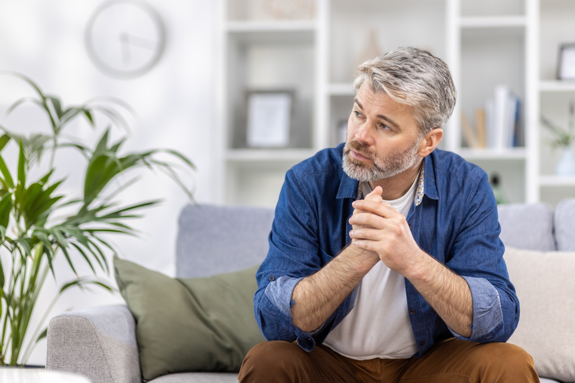 Adult mature man pensive sitting alone at home on sofa close up, gray haired person thinks looks